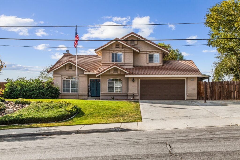 Spacious two-story house in Yucaipa, CA with a well-maintained lawn, attached garage, and American flag, perfect for families under $500,000.