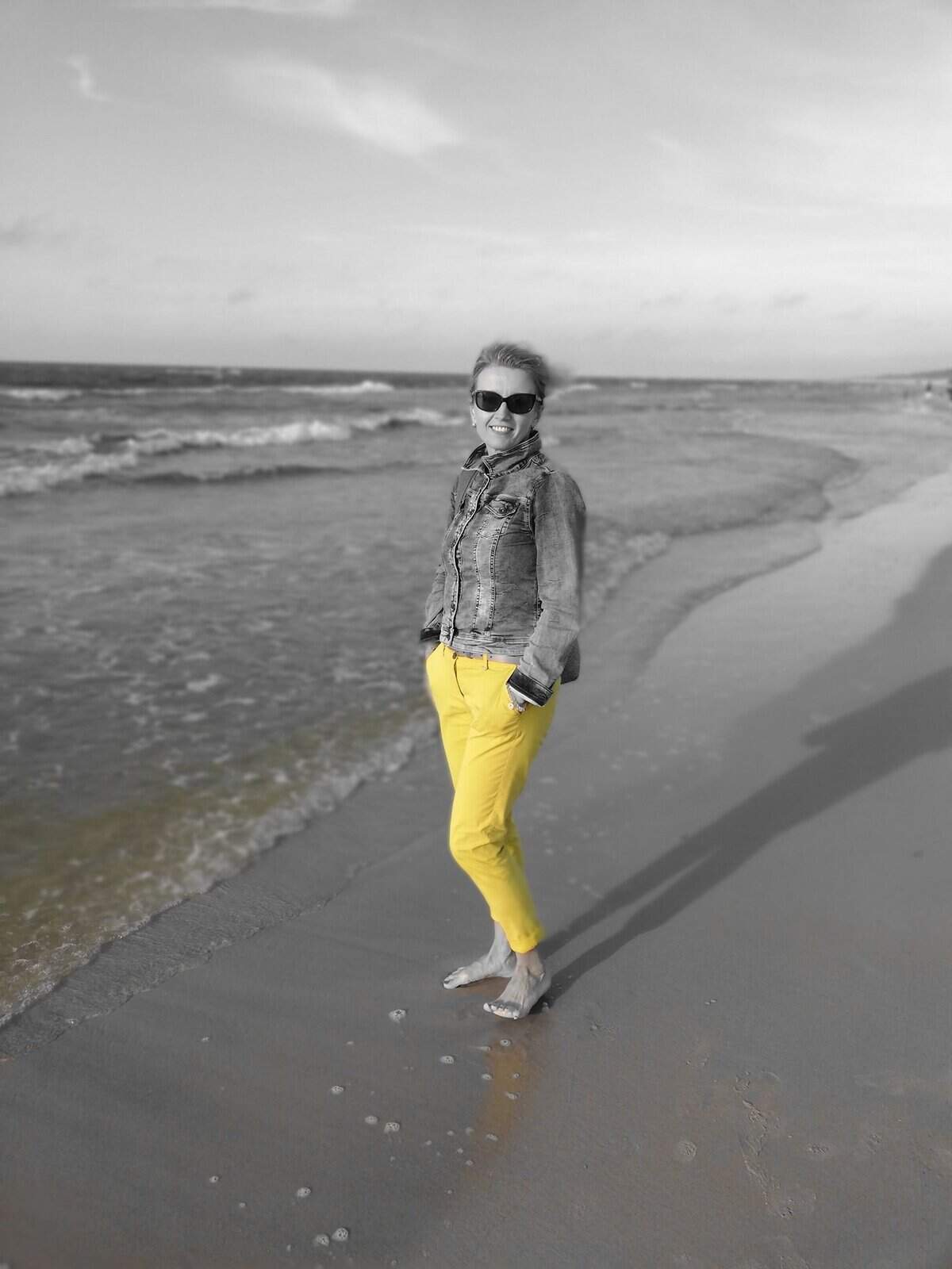Kobieta na plaży, uśmiechnięta, w słoneczny dzień, w casualowym stroju.