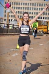 Bright female runner crossing finish line at Rock City Running event with enthusiasm and energy.