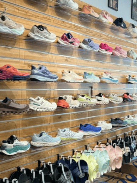 Colorful athletic shoes displayed on wooden wall shelves at Rock City Running store, featuring a wide selection of running shoes and athletic footwear.