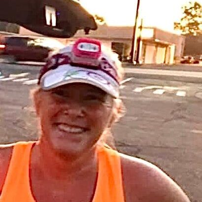 Bright female runner smiling after a race, wearing an orange tank top and running gear, with a sunset background at Rock City Running.