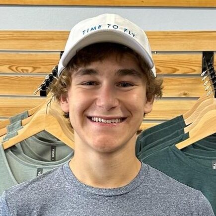 Bright smiling teenage boy wearing a "Time to Fly" cap at Rock City Running store, surrounded by activewear.