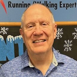A smiling man in a blue running jacket standing in front of a winter-themed backdrop at Rock City Running, your local Little Rock running and walking store with online shopping options.