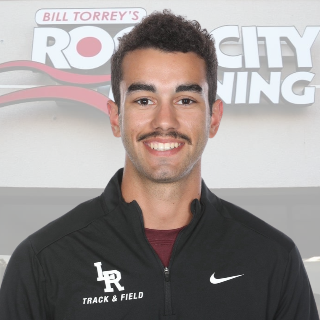 Young man in athletic apparel smiling at Rock City Running store, featuring track and field gear and running shoes, promoting sportswear and athletic training.