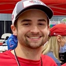 High-energy runner smiling at Rock City Running event with vibrant outdoor setting and branded attire, showcasing athletic gear and community engagement.