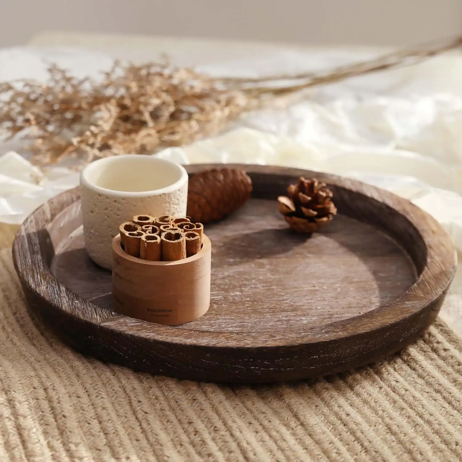Wooden tray with cinnamon sticks, pine cone, and mug for cozy home decor.
