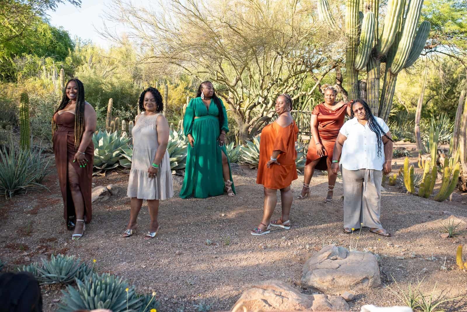 Group of women standing in a desert garden with cacti and succulents, enjoying a sunny day.