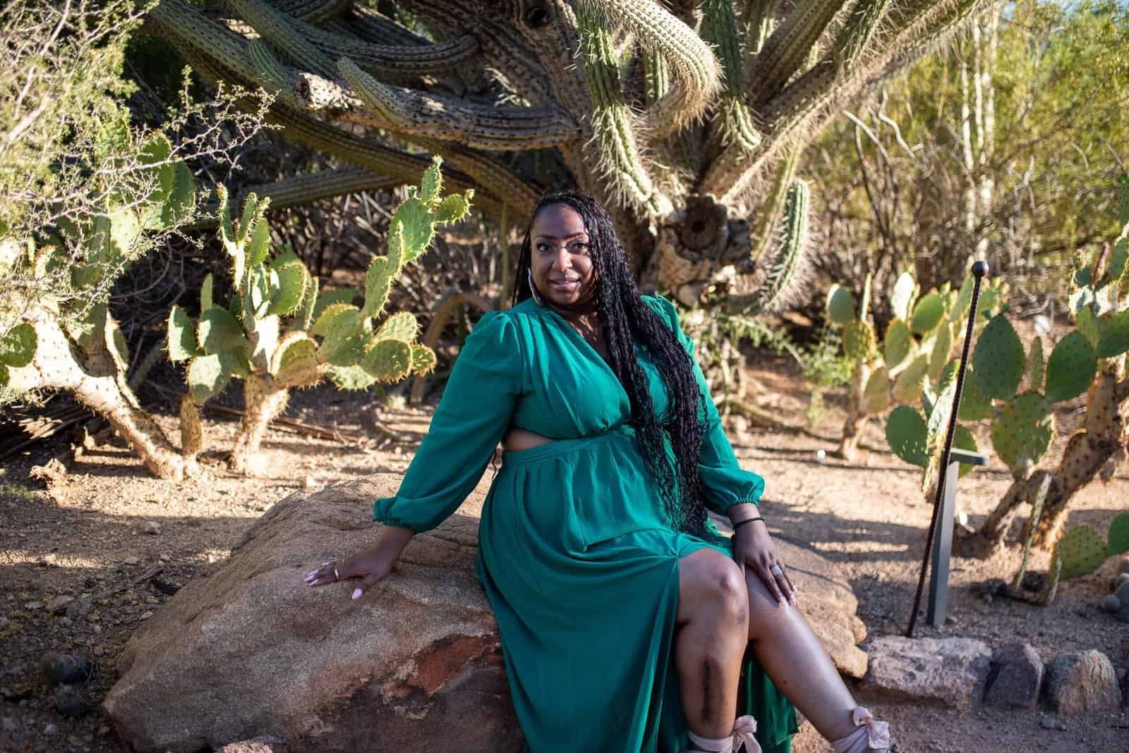 A woman in a teal dress relaxing outdoors among desert plants and cacti, capturing a special moment.