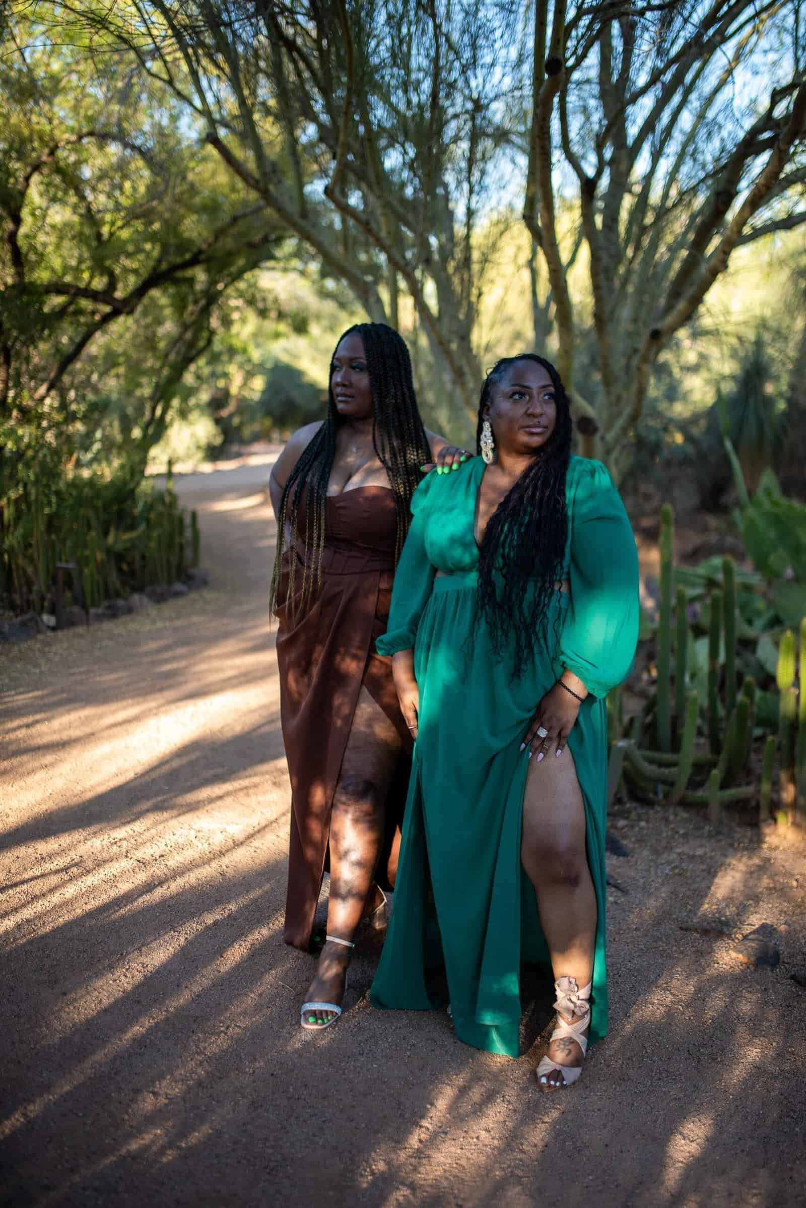 Two women in stylish dresses strolling through a scenic garden, capturing a moment of elegance and friendship.