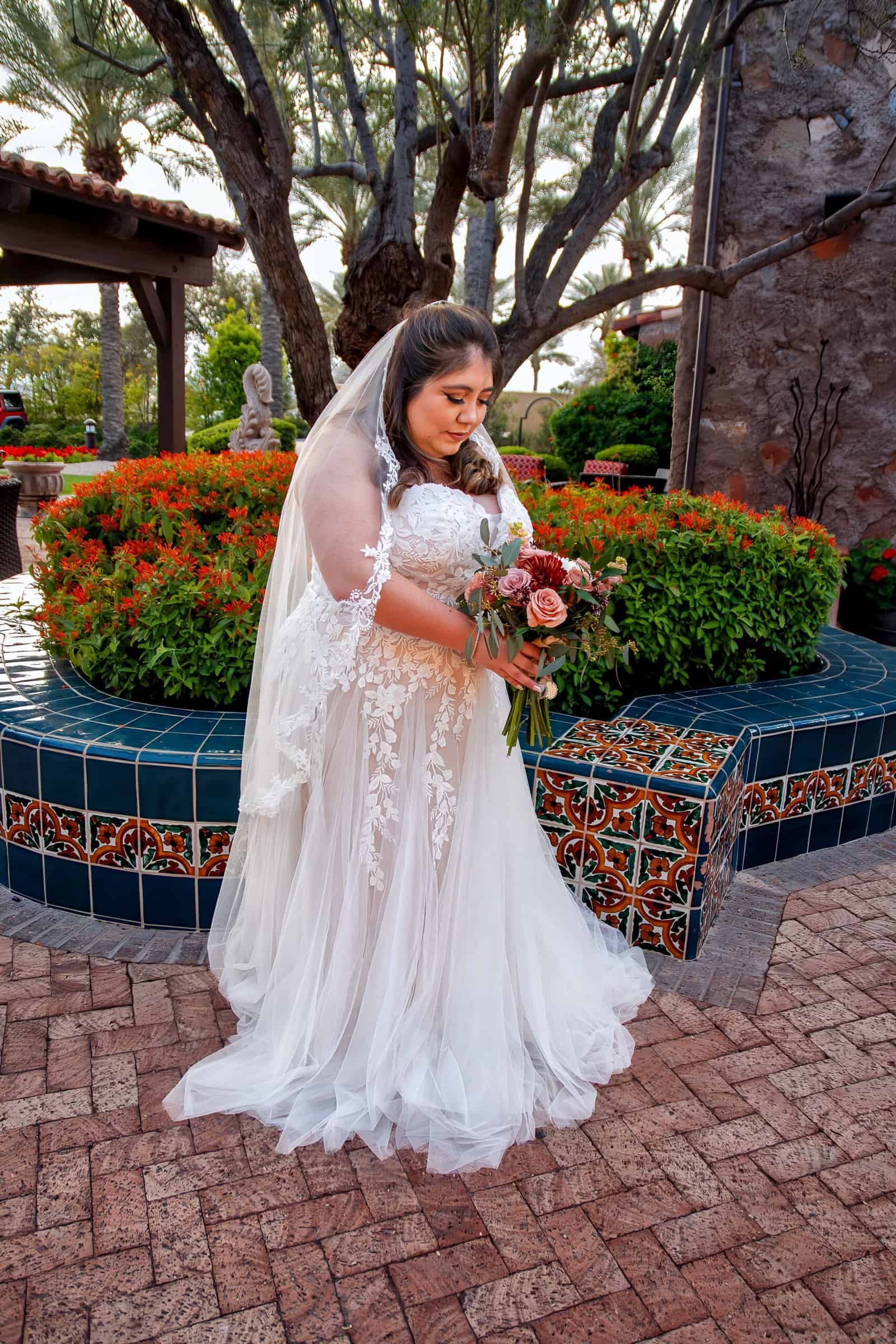 Beautiful bride in wedding dress with bouquet, outdoors at a garden fountain, perfect for wedding photography.