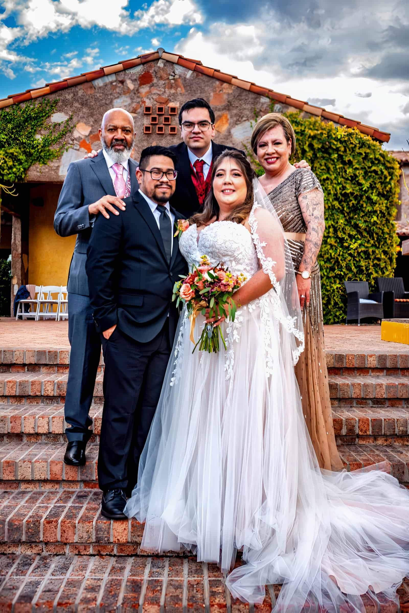 Joyful wedding photo capturing the bride, groom, and family in front of a rustic house.