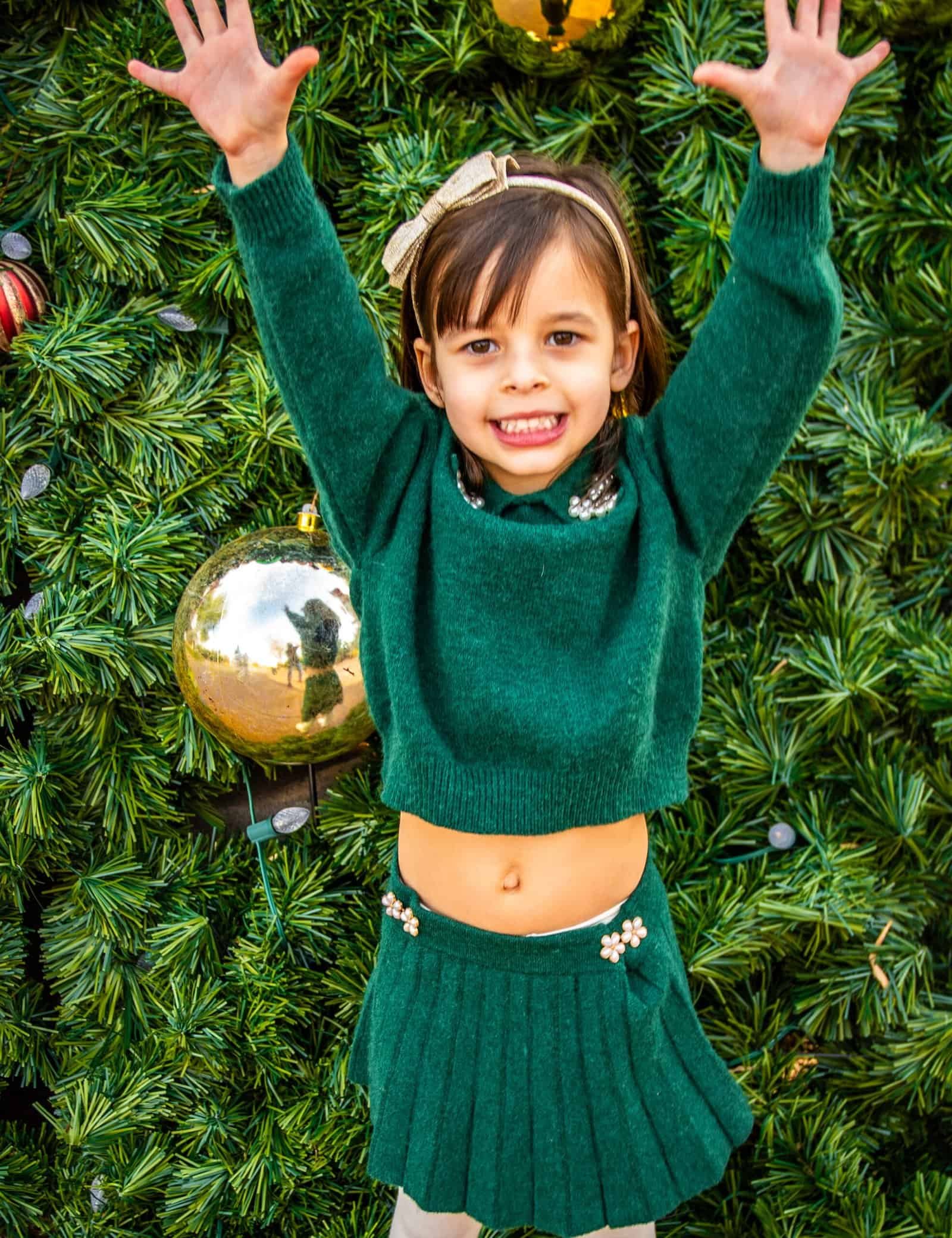 Happy young girl in green sweater and skirt celebrating Christmas holiday cheer.
