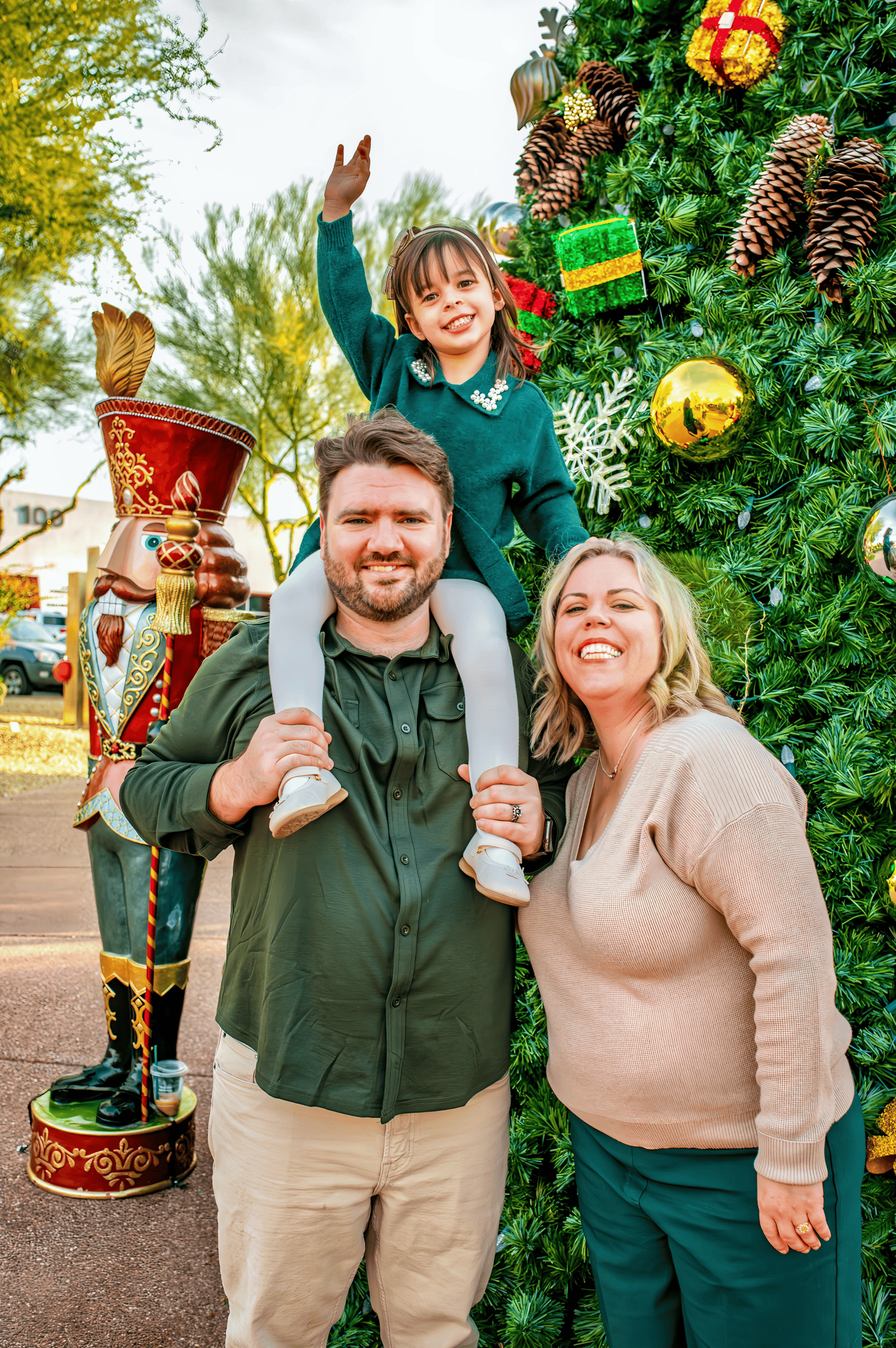 Joyful family photo with parents and child near Christmas tree outdoors.