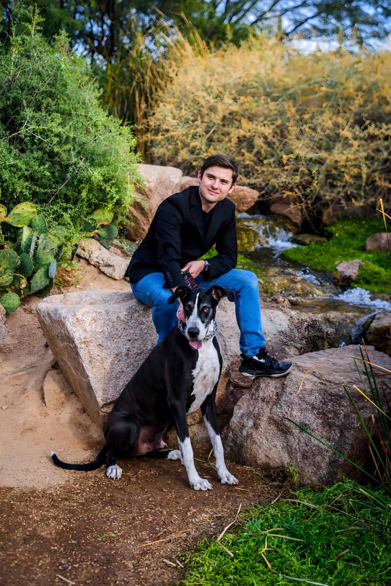Man enjoying a peaceful moment with his dog by a stream in a scenic outdoor park.