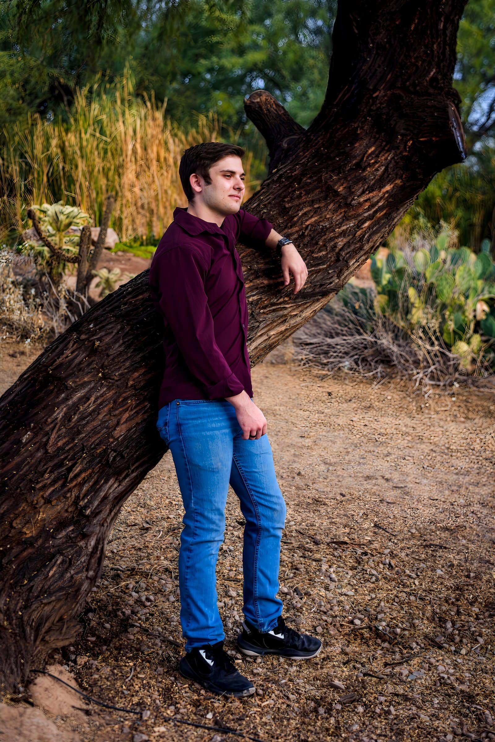 Portrait of a young man standing by a tree in a lush, green outdoor landscape, capturing a peaceful moment.