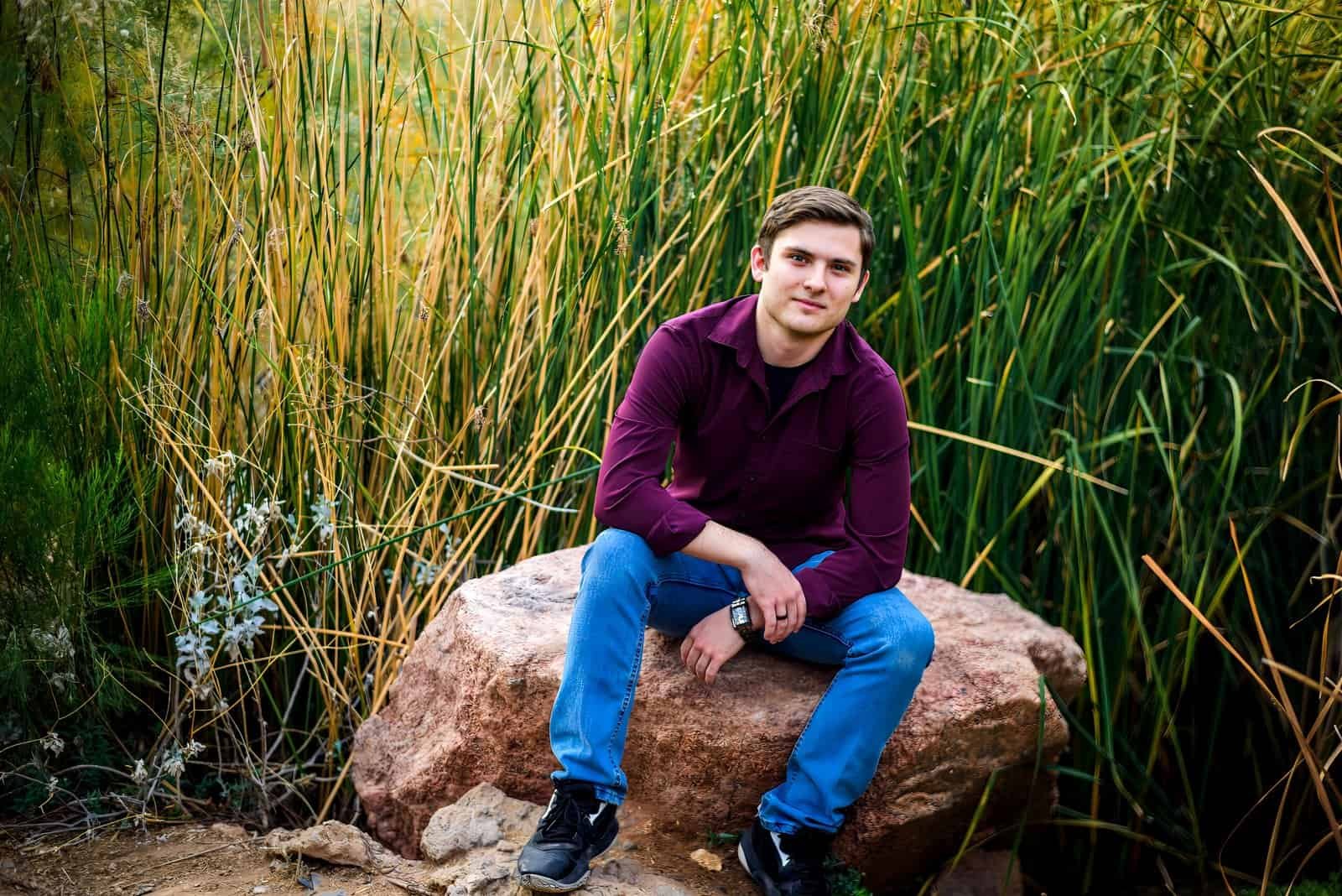 Portrait of a young man relaxing outdoors on a rock amidst lush greenery and natural scenery.
