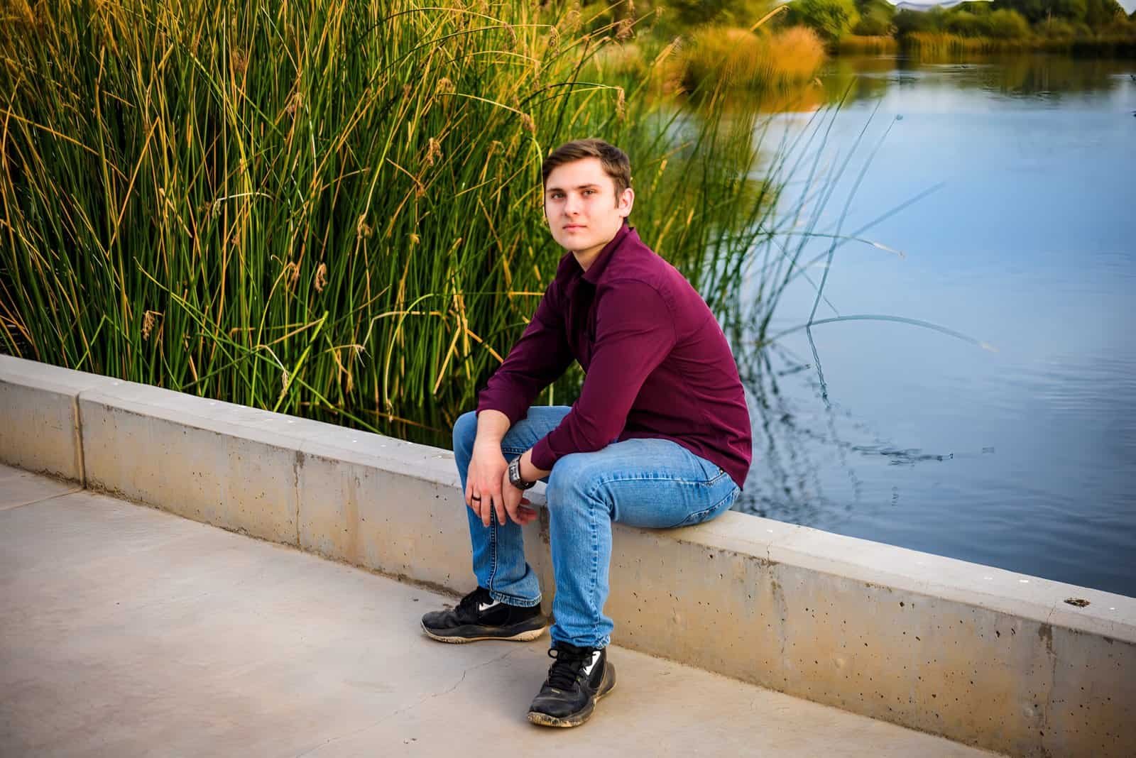 A young man relaxing by a serene lake during sunset, capturing a moment of tranquility and reflection.