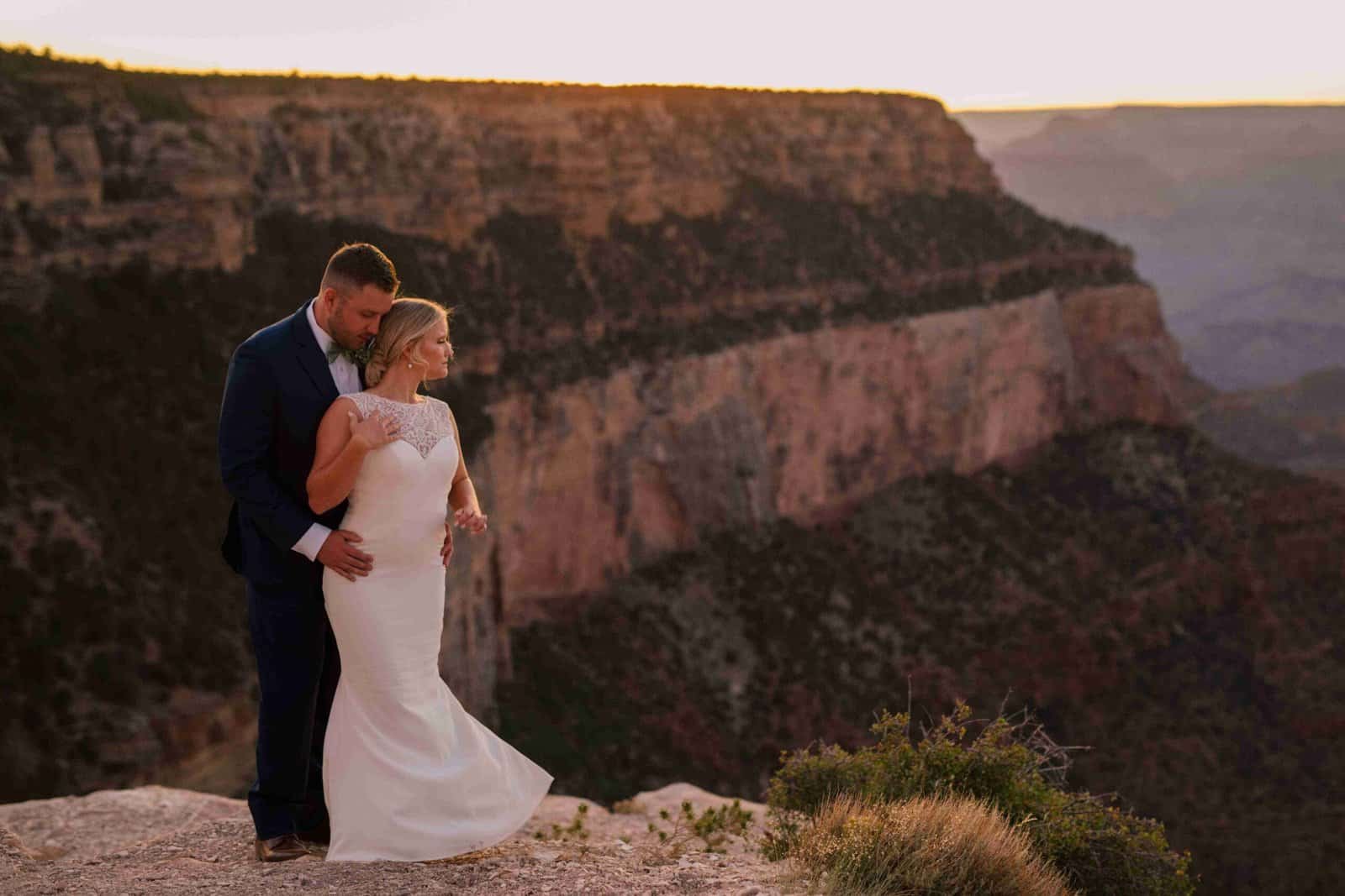 A bride and groom share a romantic moment at the Grand Canyon during sunset, capturing a beautiful and memorable wedding scene.