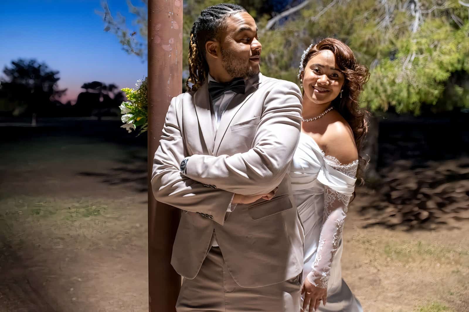 A stylish couple dressed in formal wear sharing a joyful moment in a scenic outdoor setting during sunset.