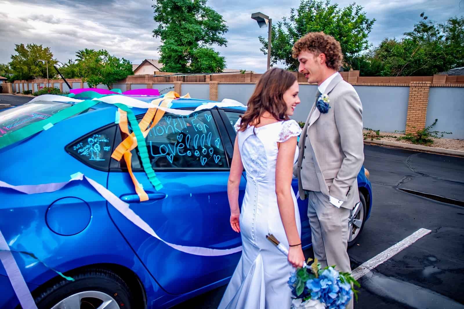 Bride and groom sharing a joyful moment next to a decorated wedding car.