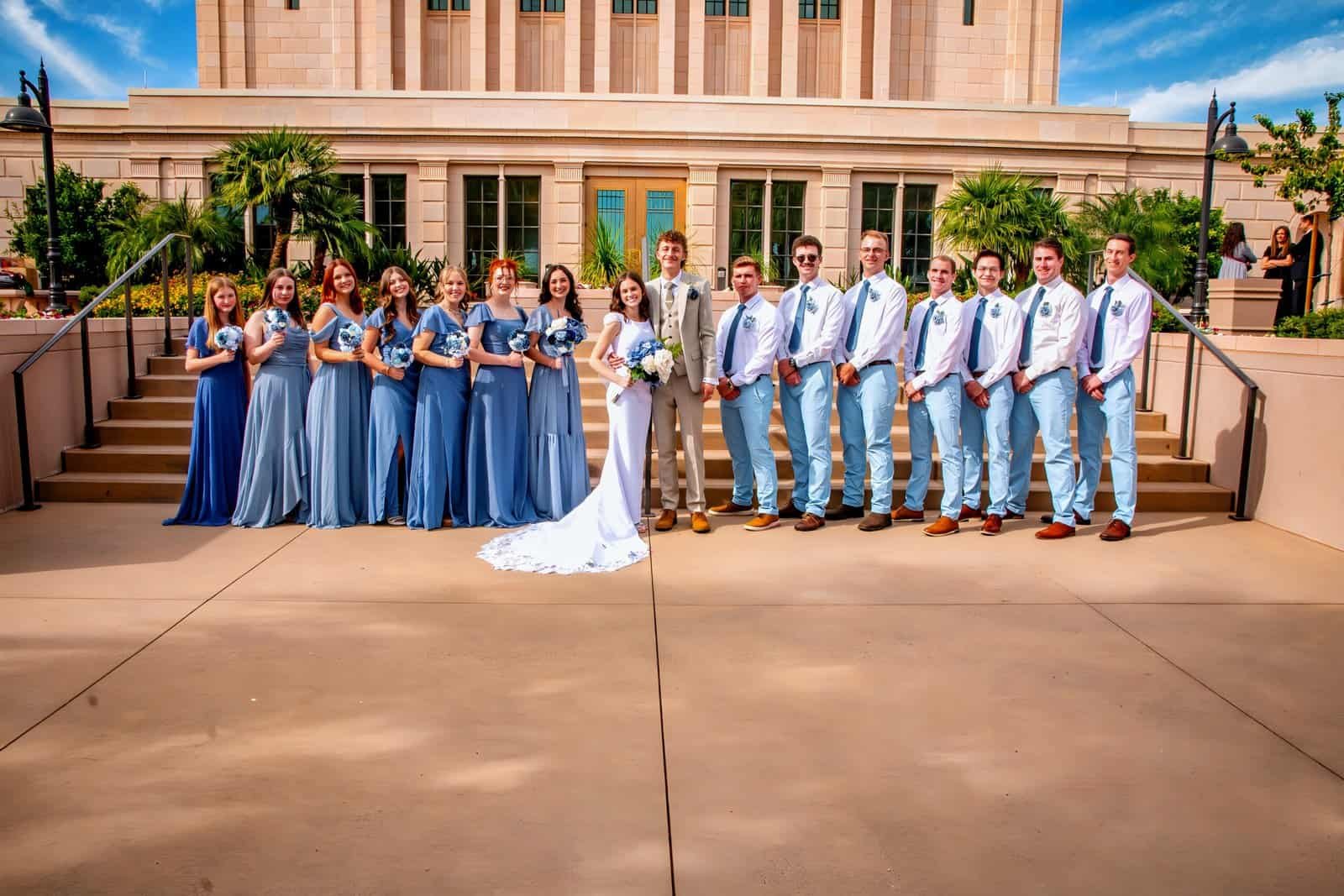 A joyful wedding celebration with the bride, groom, bridesmaids, and groomsmen posing on steps in front of a historic building.