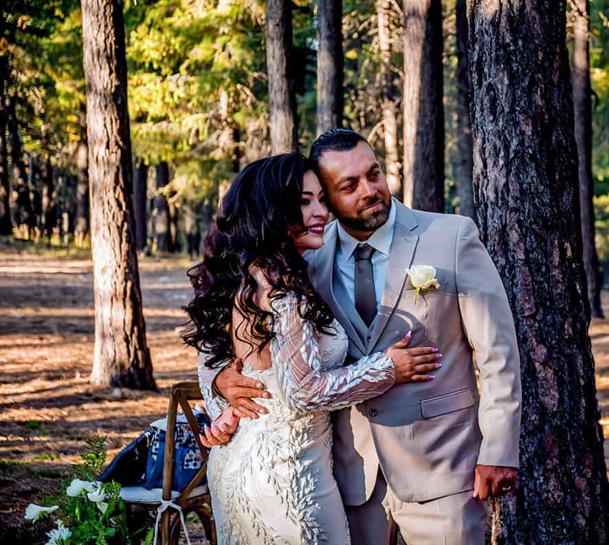 A bride and groom share a tender moment in a wooded area, highlighting their love and joy on their special day.