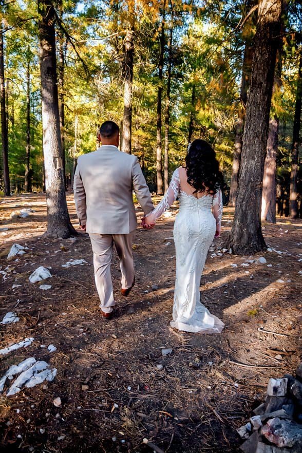 A bride and groom walk together through a sunlit forest, capturing a romantic moment on their wedding day amidst nature's beauty.