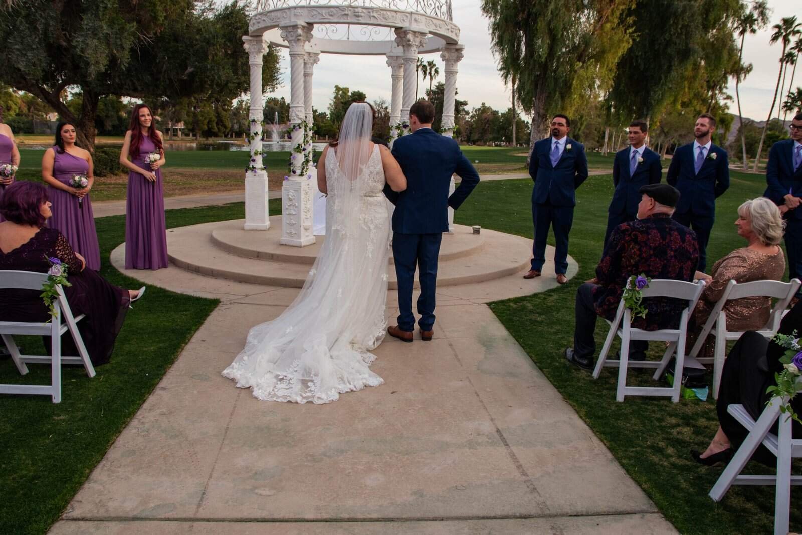 Beautiful outdoor wedding ceremony with bride and groom, officiant, and guests in a scenic garden setting.