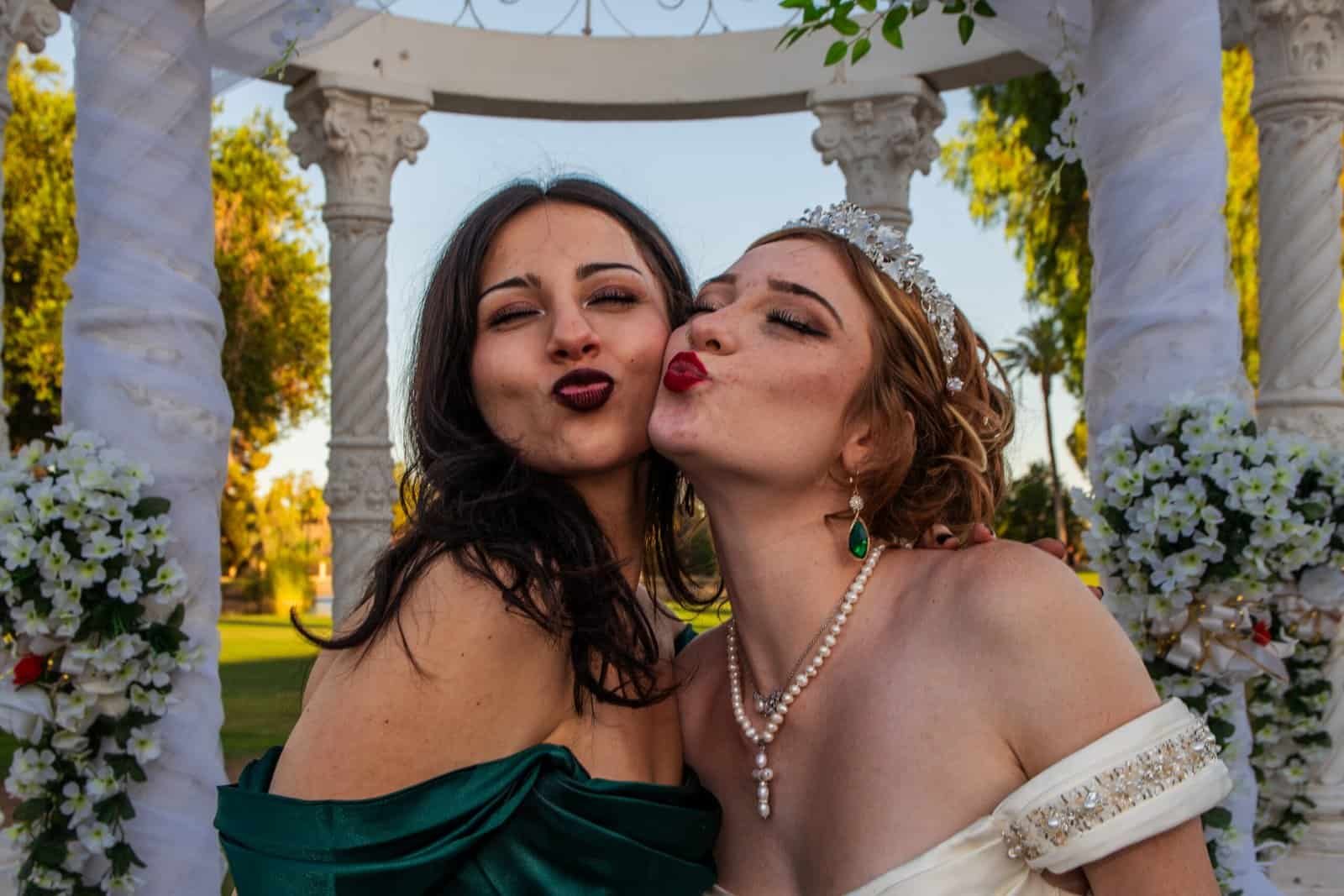 Two women kissing and celebrating at a wedding or special occasion outdoors.