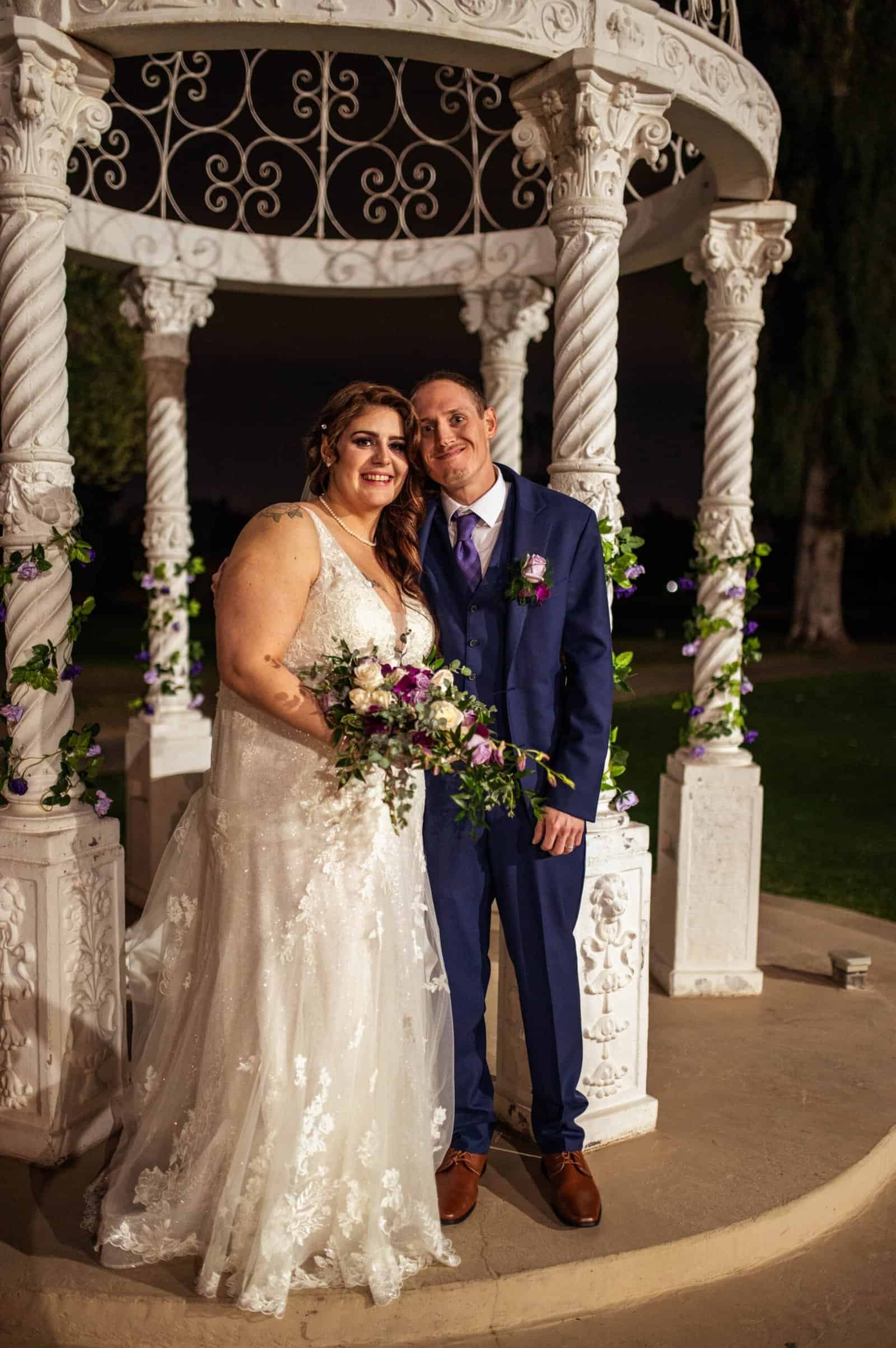 A joyful bride and groom pose together at their wedding ceremony, surrounded by romantic decor and lush greenery.