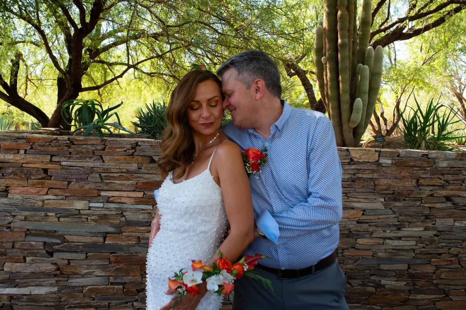 A bride and groom share a tender moment outdoors, surrounded by lush greenery and cacti, celebrating their wedding day.