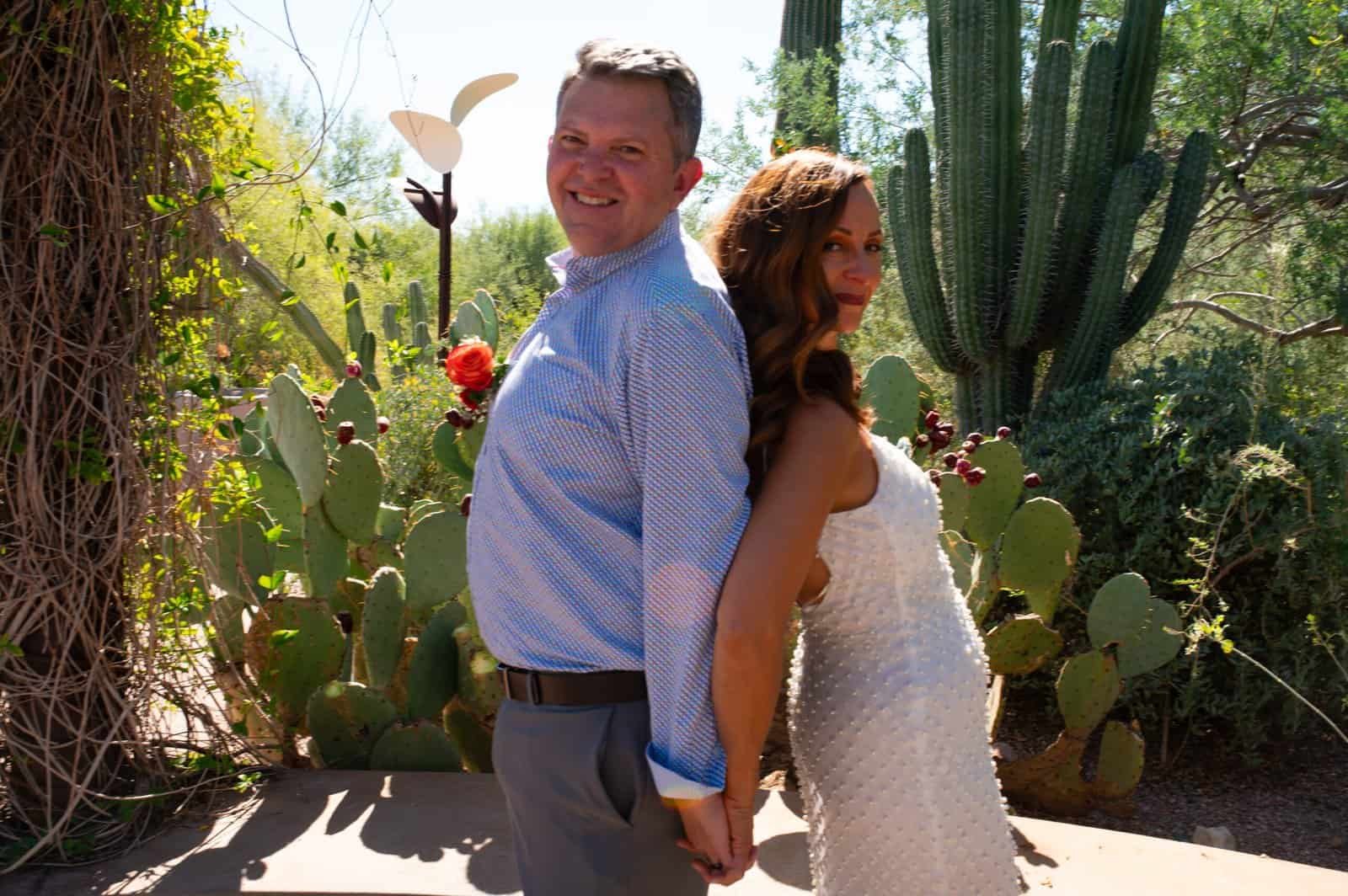 A happy couple poses back-to-back in a desert garden filled with cacti and succulents, celebrating their special day.