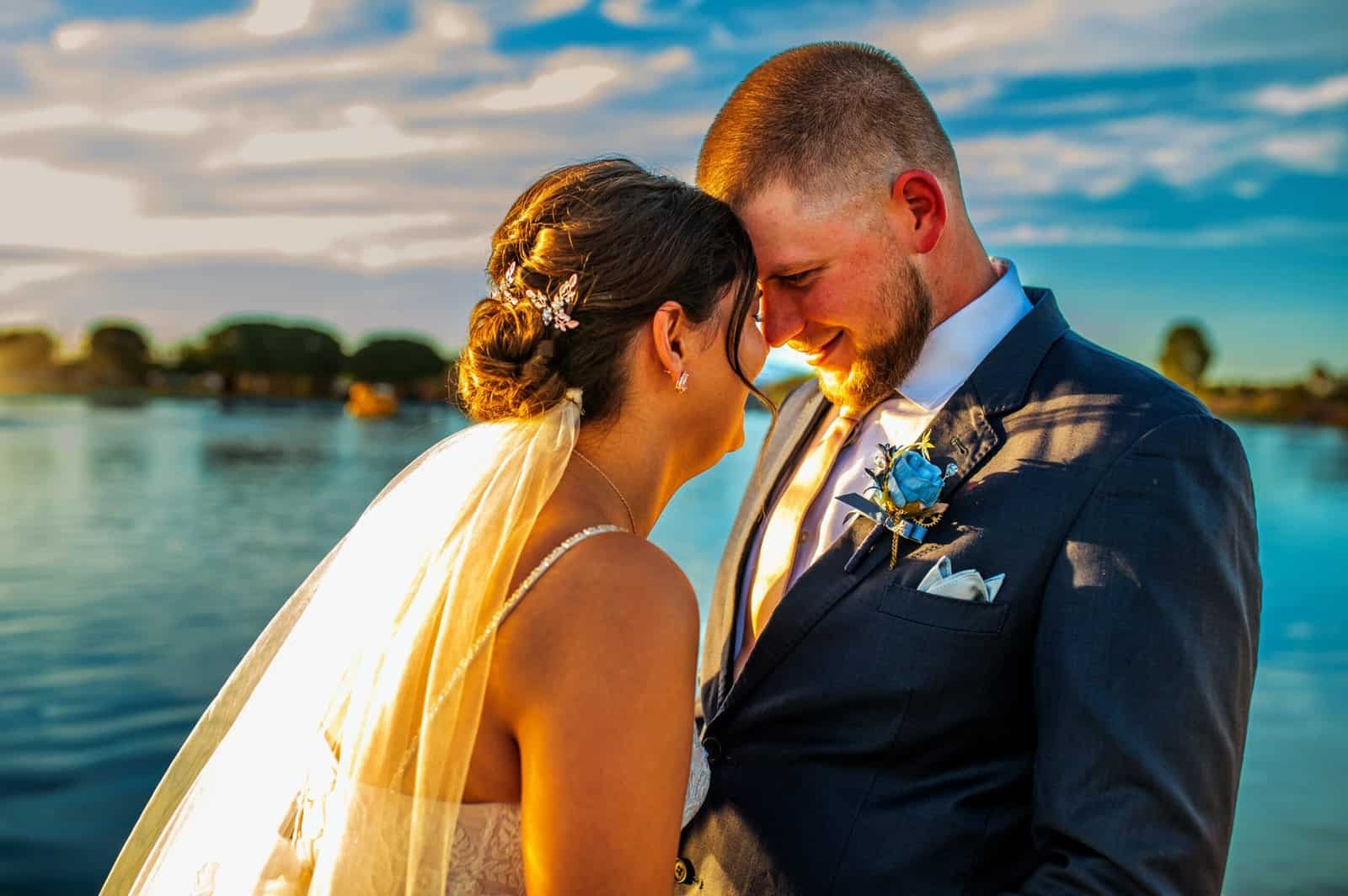 Beautiful wedding moment with a bride and groom sharing an intimate embrace by the water at sunset.