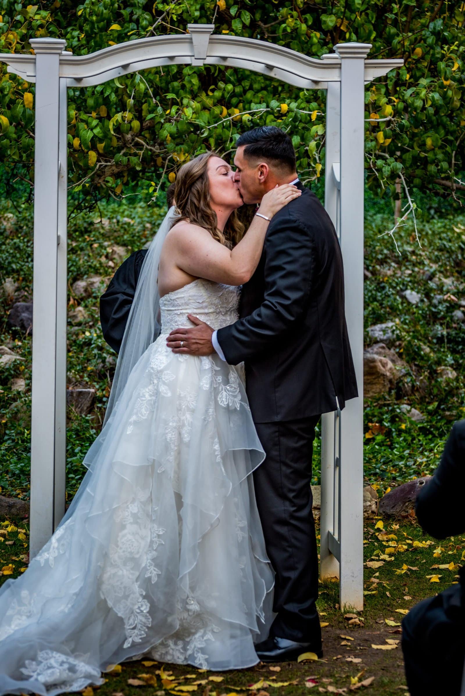 Beautiful outdoor wedding moment featuring a bride and groom sharing a kiss under a floral arch.