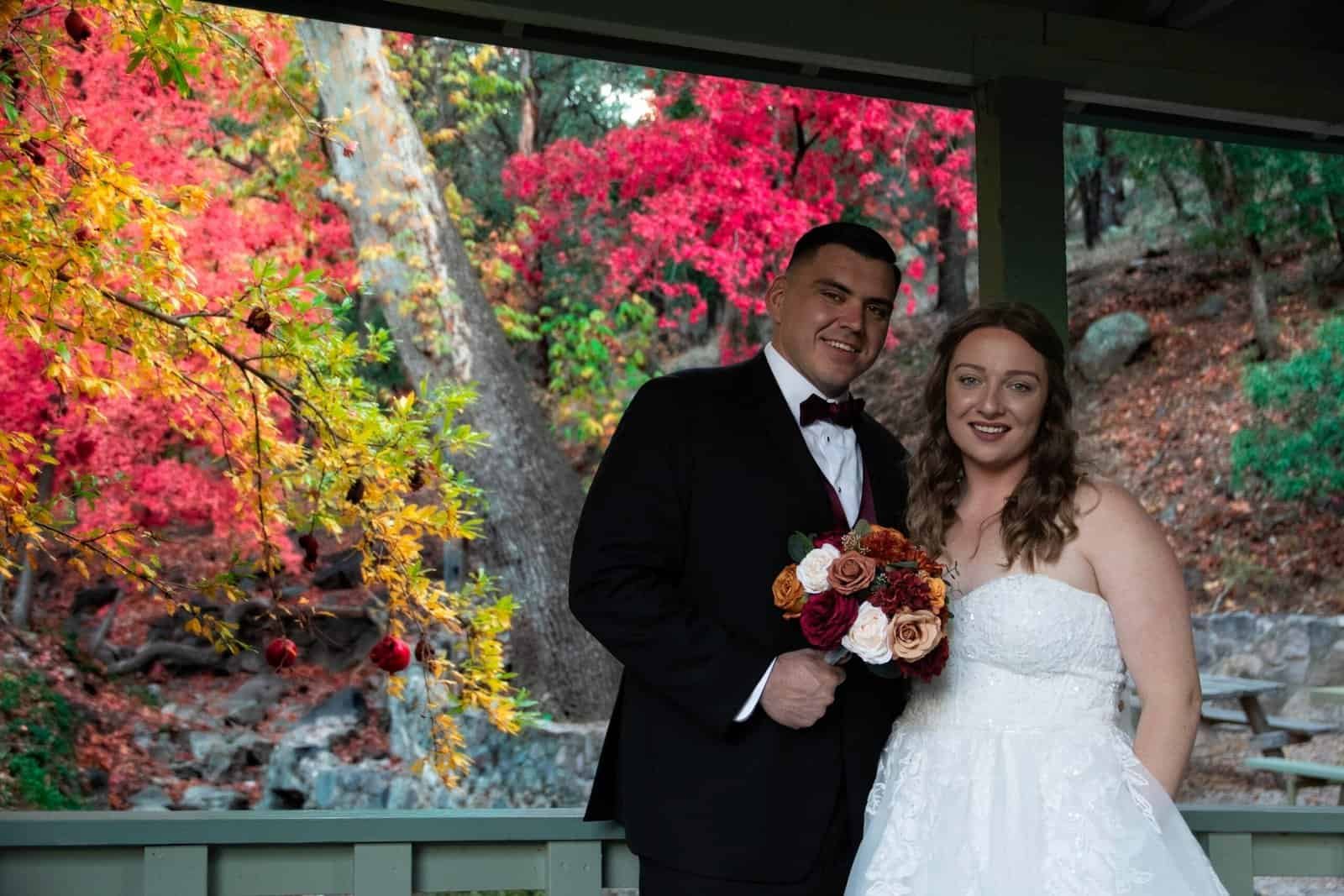 Beautiful bride and groom posing together in a scenic autumn setting, capturing a special moment on their wedding day.