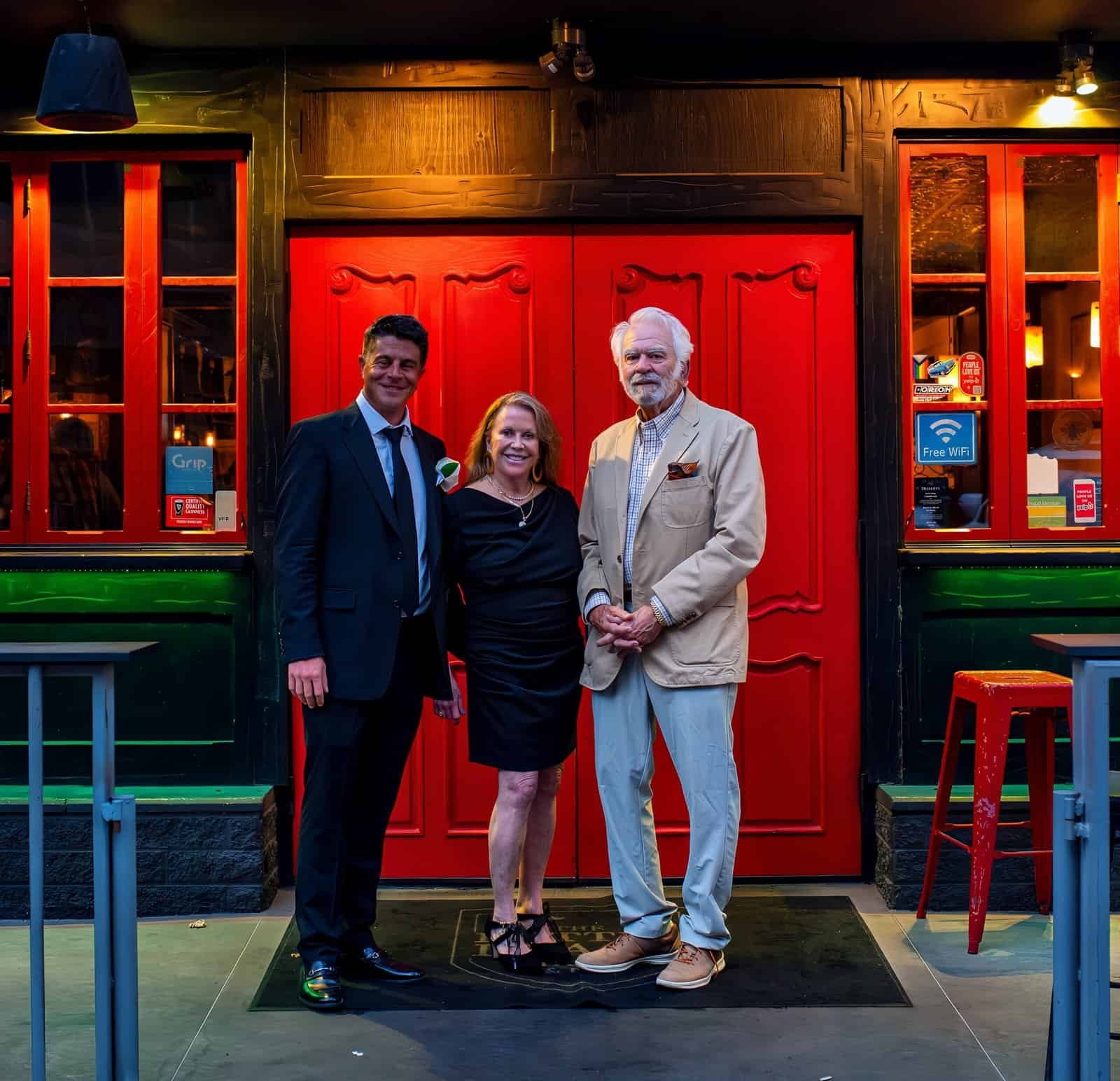Three individuals dressed formally, standing together outside a vibrant restaurant entrance, celebrating a special occasion.