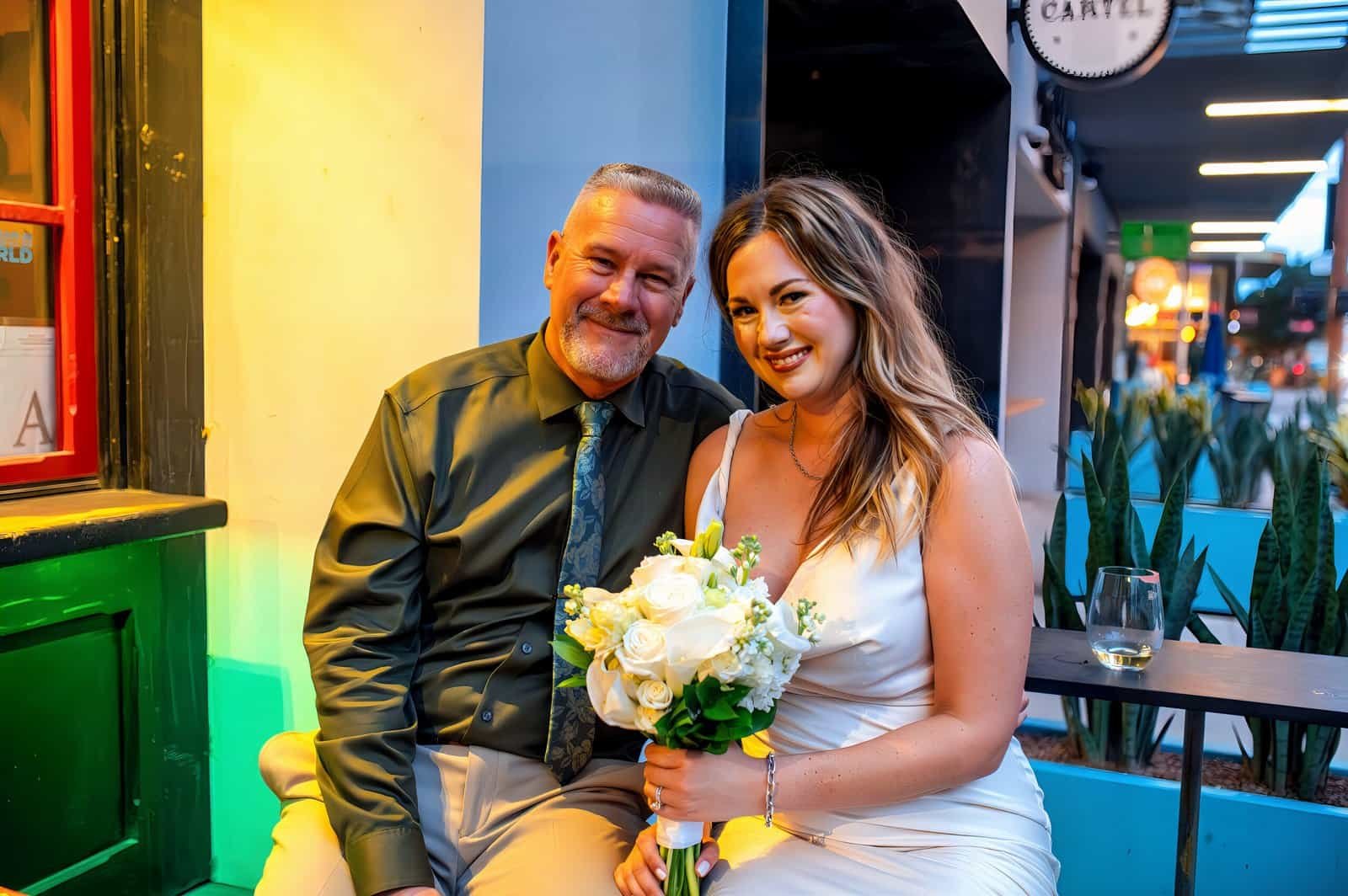 A joyful bride and a man celebrating at a wedding reception, capturing a happy moment with colorful lighting and festive atmosphere.