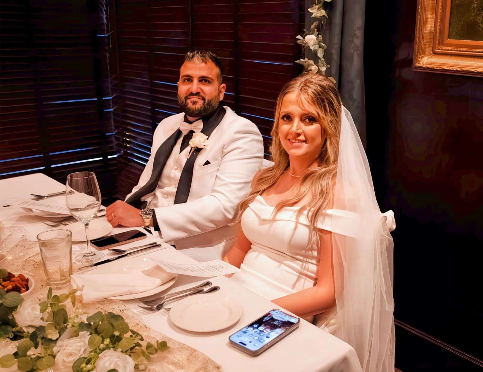 A bride and groom sit together at a beautifully decorated wedding reception, smiling and enjoying their celebration.