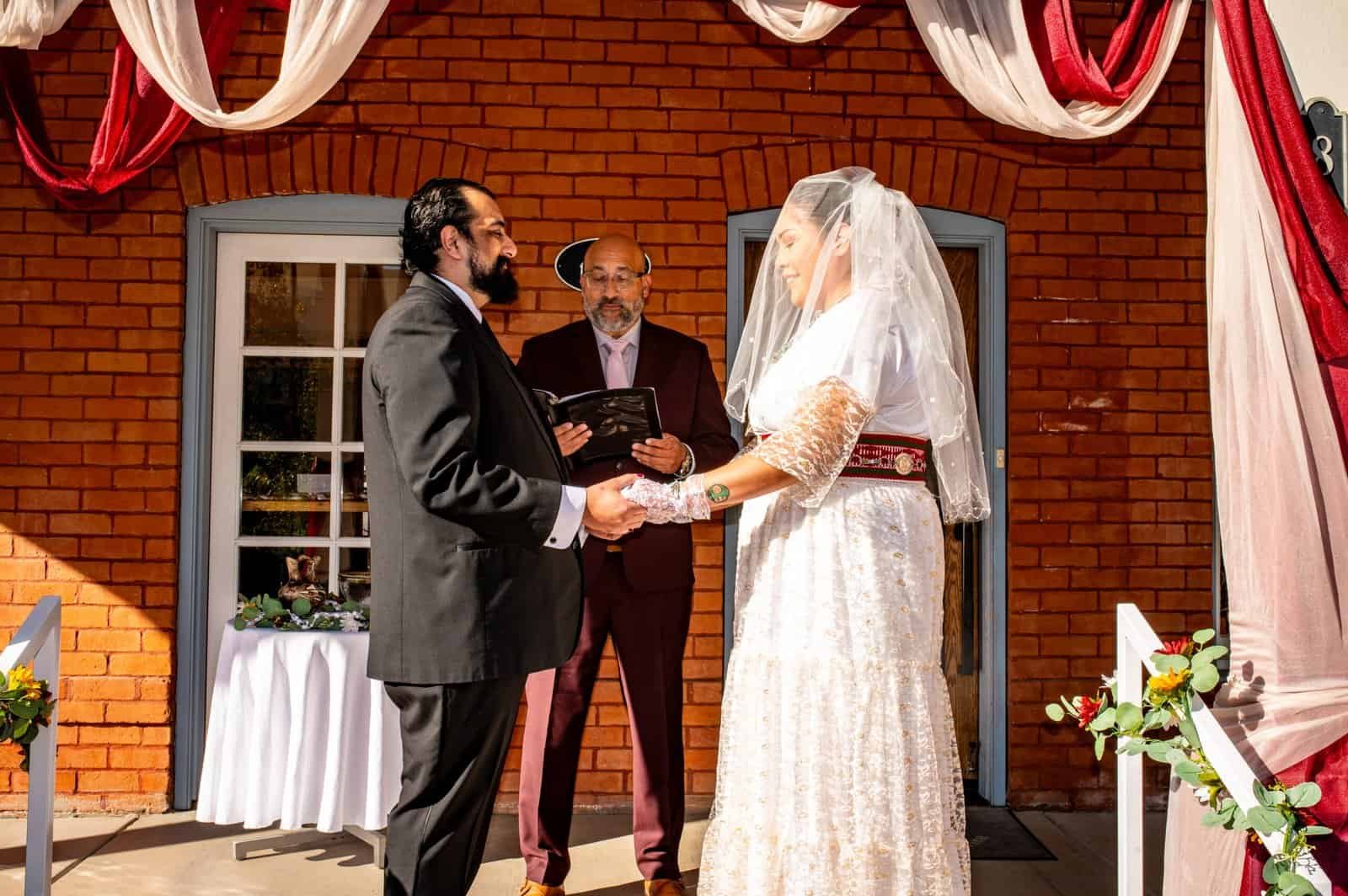 Beautiful outdoor wedding with bride and groom exchanging vows, officiant, and decorated venue.