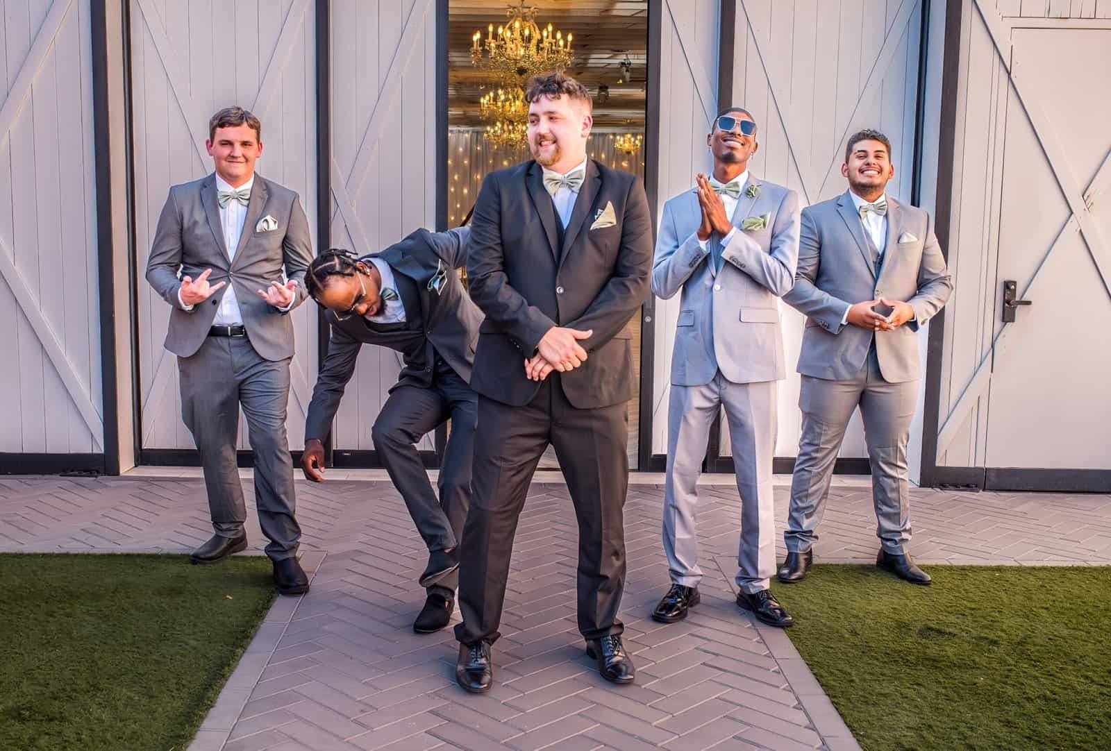 Group of groomsmen in suits enjoying a joyful moment at a wedding celebration outside.
