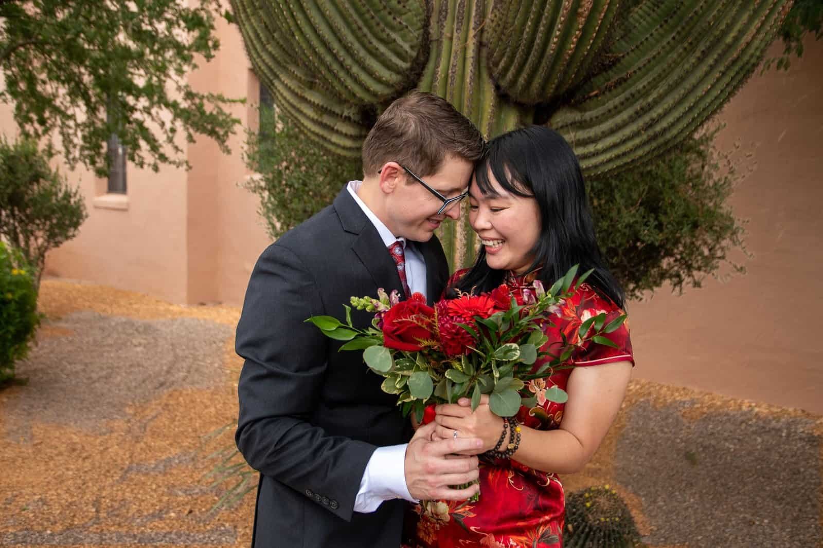 Happy wedding couple exchanging smiles and flowers in a desert garden setting.