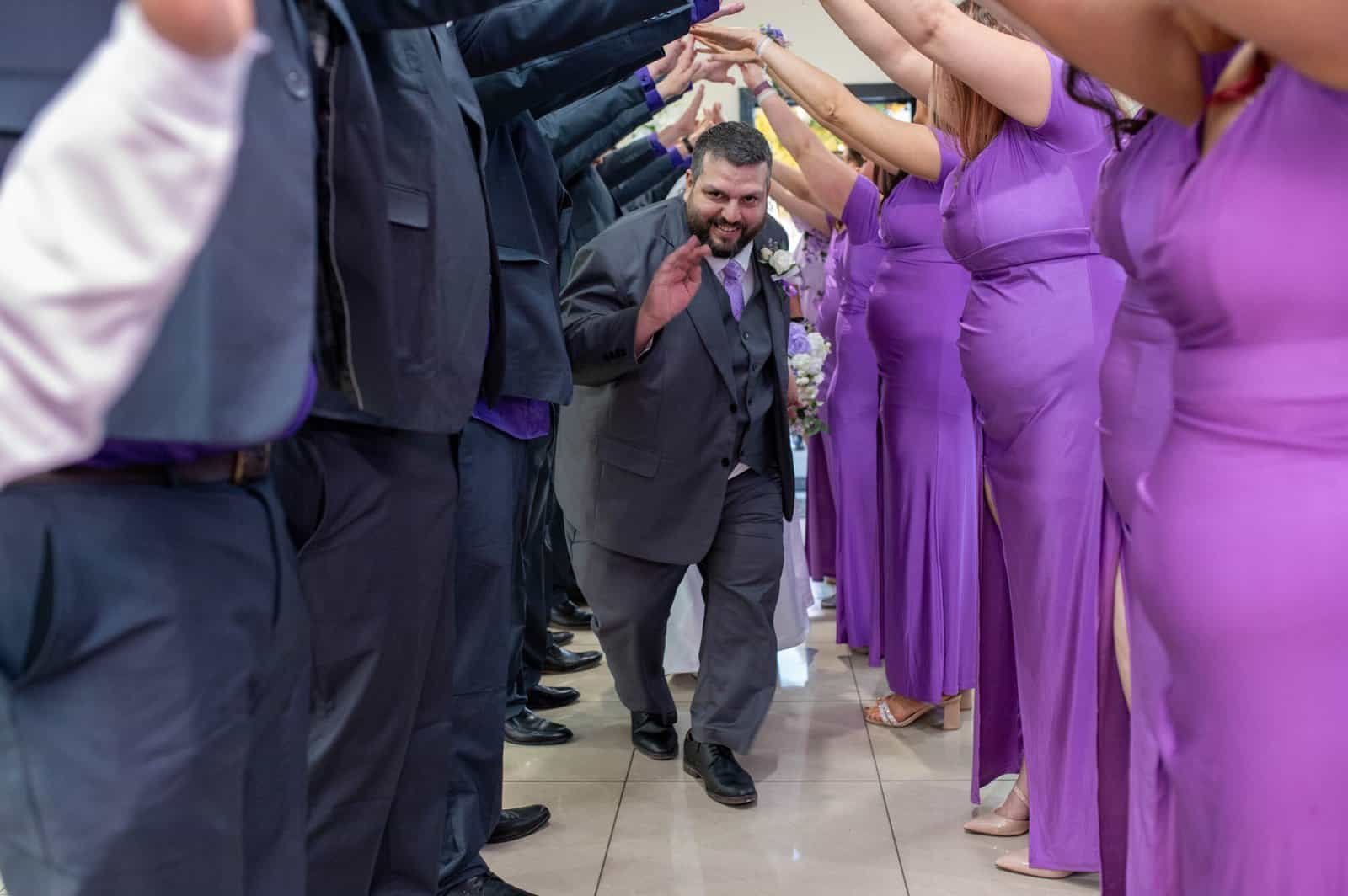 Wedding party forms a joyful tunnel as groom walks through, celebrating love and unity at the wedding reception.