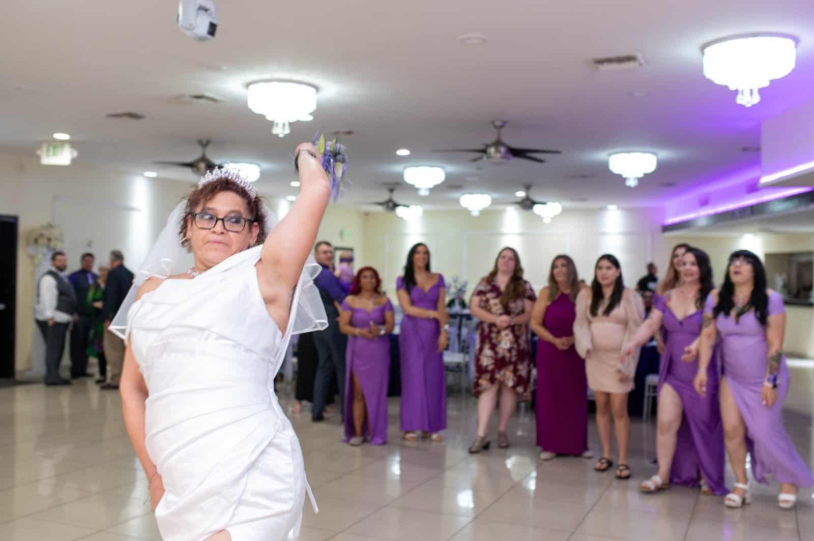 A bride in a white dress dances at her wedding reception with guests in elegant attire watching.