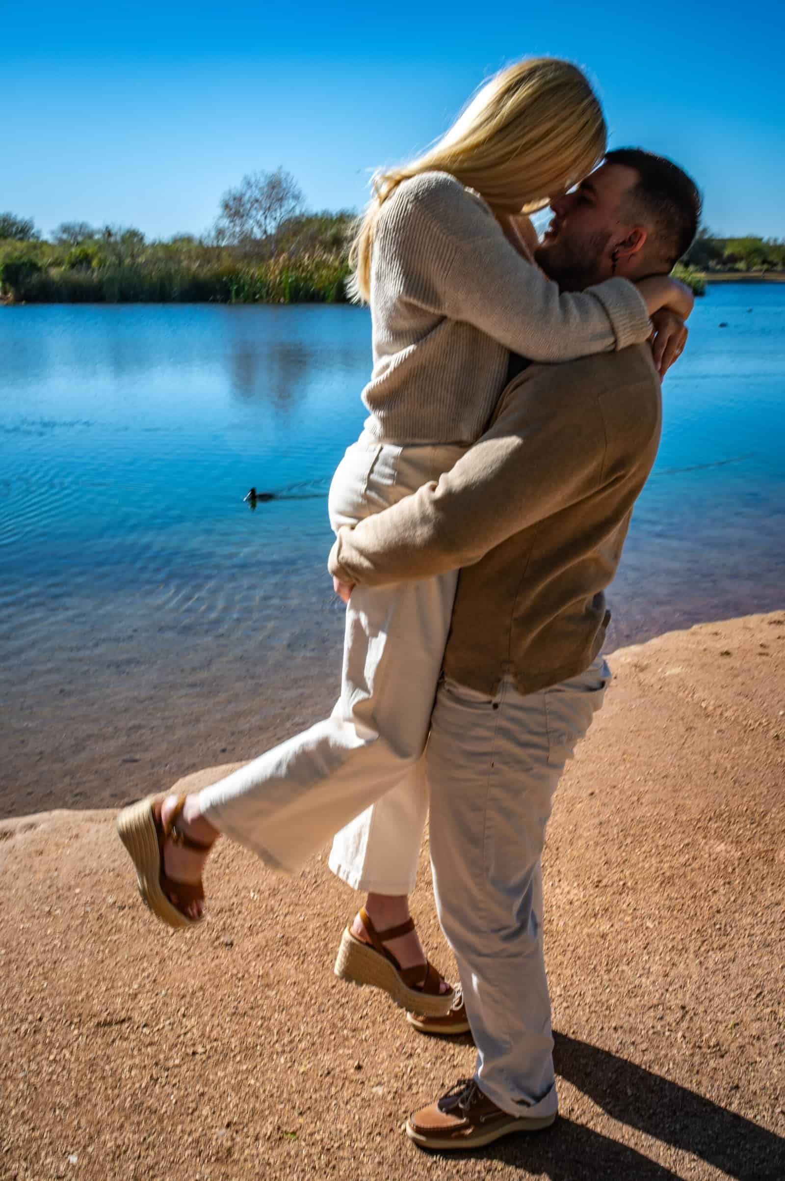 A couple sharing a romantic embrace by the water, capturing a joyful and intimate moment outdoors.