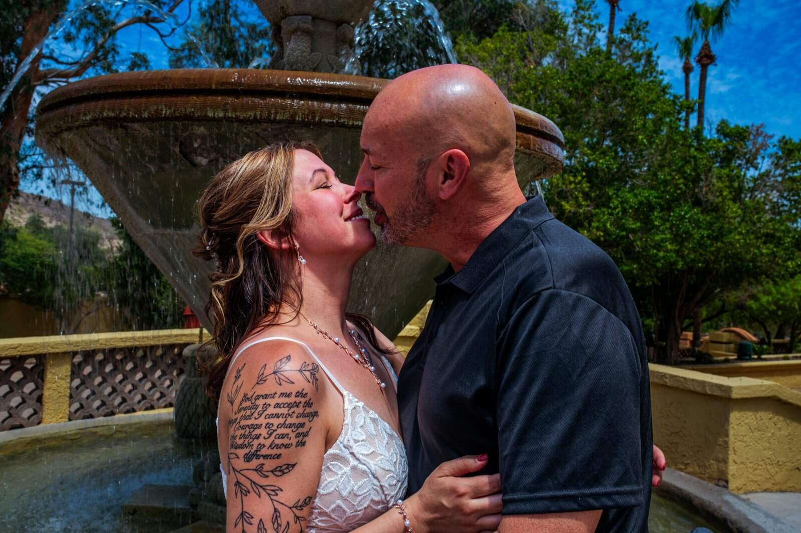 Romantic wedding moment captured outdoors with a couple kissing by a fountain, highlighting love and commitment.