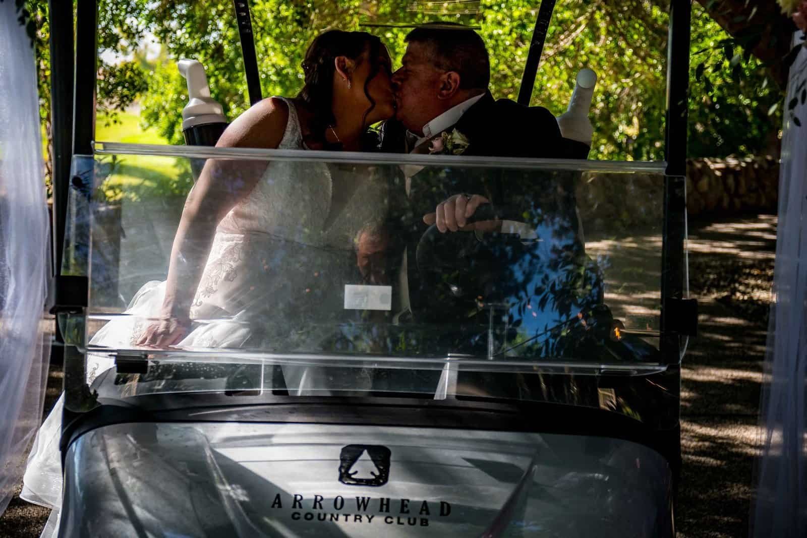 A couple shares a romantic kiss inside a golf cart at Arrowhead Country Club during their wedding celebration.