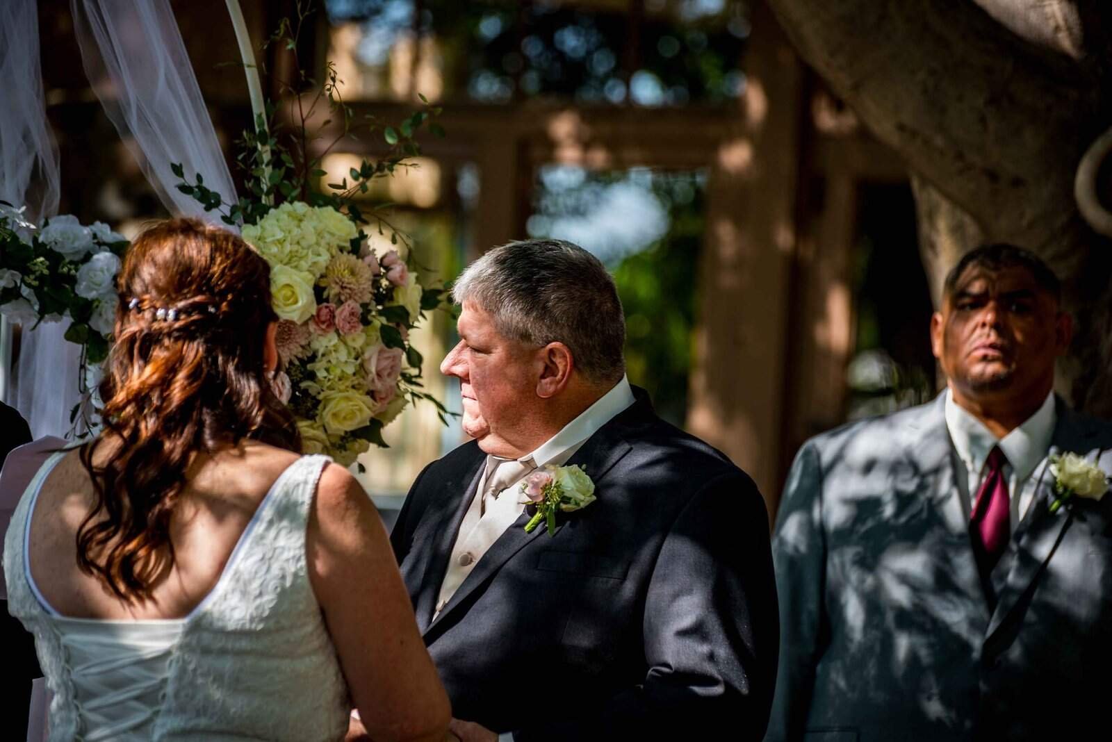 A couple shares a heartfelt moment during their outdoor wedding ceremony, with an officiant and scenic natural background.