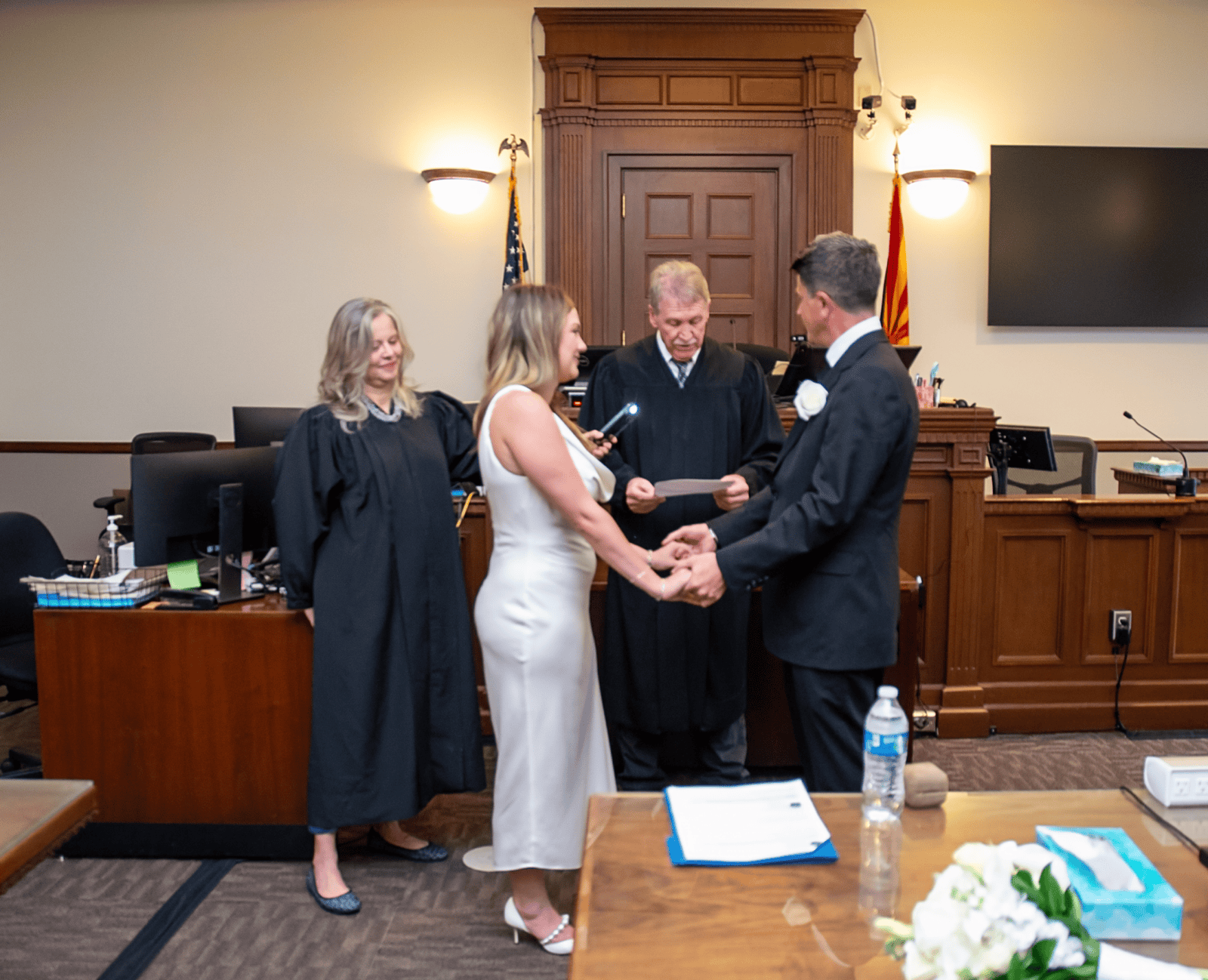 Couple getting married in a courthouse, holding hands during the vows with officiant present.