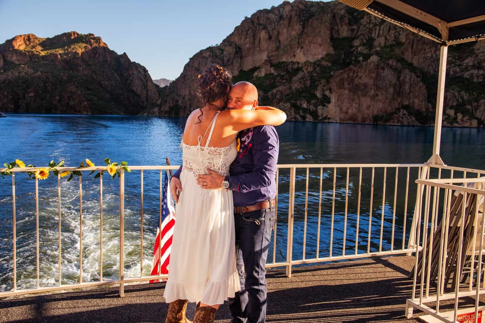 A loving couple shares a heartfelt embrace on a boat cruise, enjoying stunning views of the lake and mountains during sunset.
