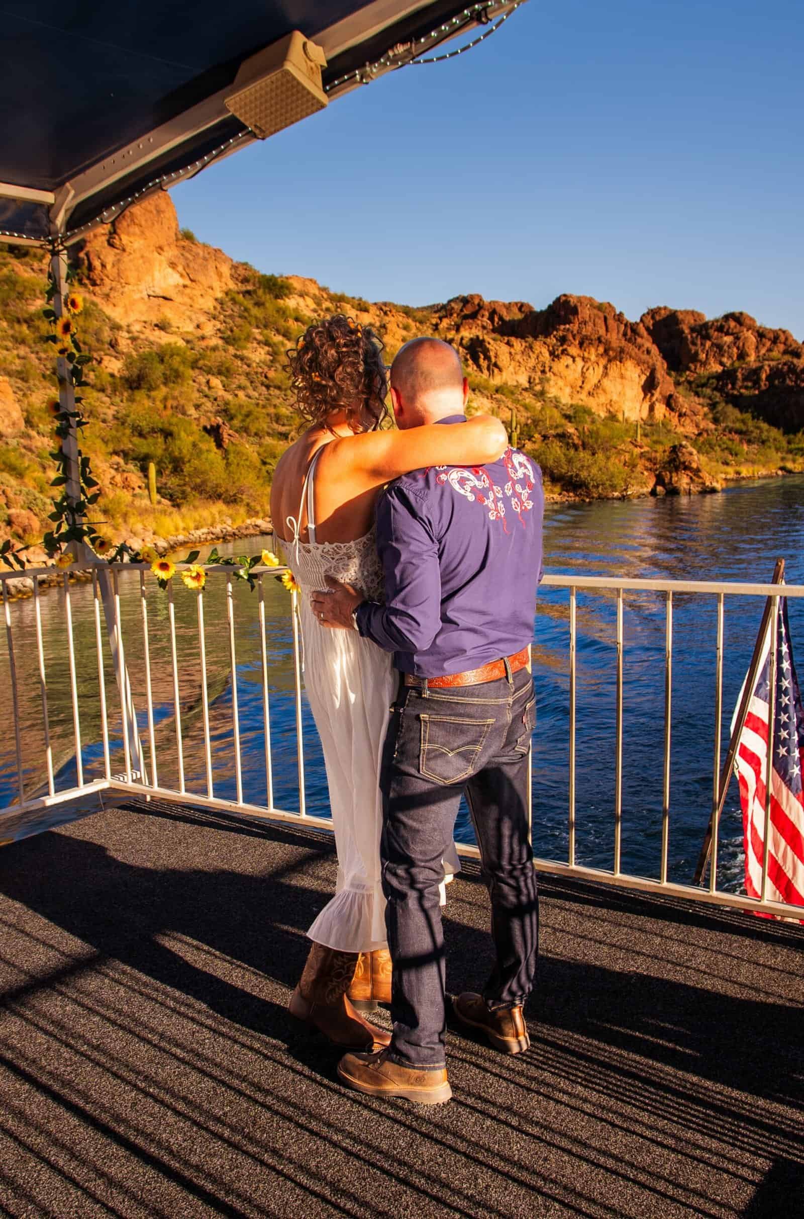 A couple enjoying a romantic moment on a boat, embracing with scenic cliffs and water at sunset, capturing love and adventure.